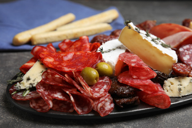 Photo of Tasty salami and other delicacies served on grey table, closeup