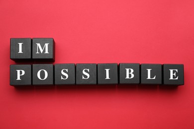 Photo of Motivation concept. Changing word from Impossible into Possible by removing black wooden cubes on red background, flat lay
