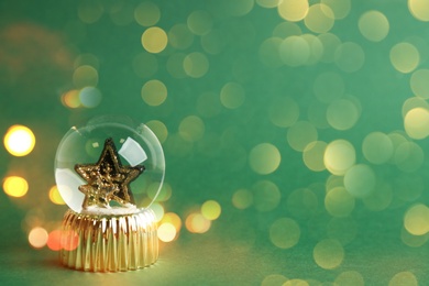 Beautiful Christmas snow globe with small star on green background, bokeh effect. Space for text