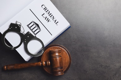 Photo of Judge's gavel, handcuffs and Criminal law book on grey background, flat lay. Space for text