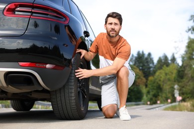 Photo of Tire puncture. Man checking wheel of car on roadside outdoors