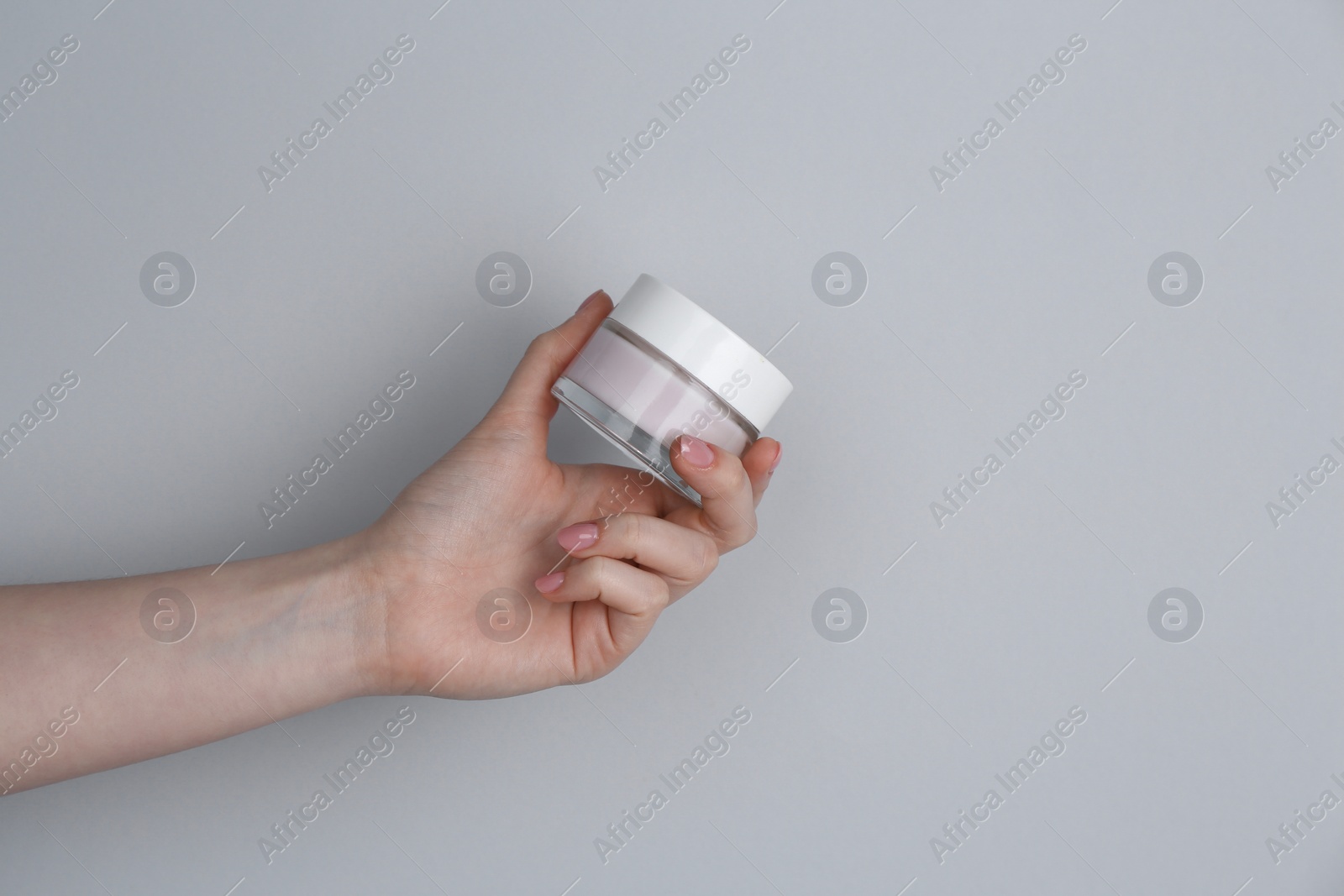 Photo of Woman holding jar of cream on grey background, closeup. Space for text