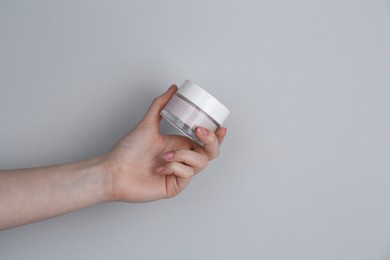 Woman holding jar of cream on grey background, closeup. Space for text