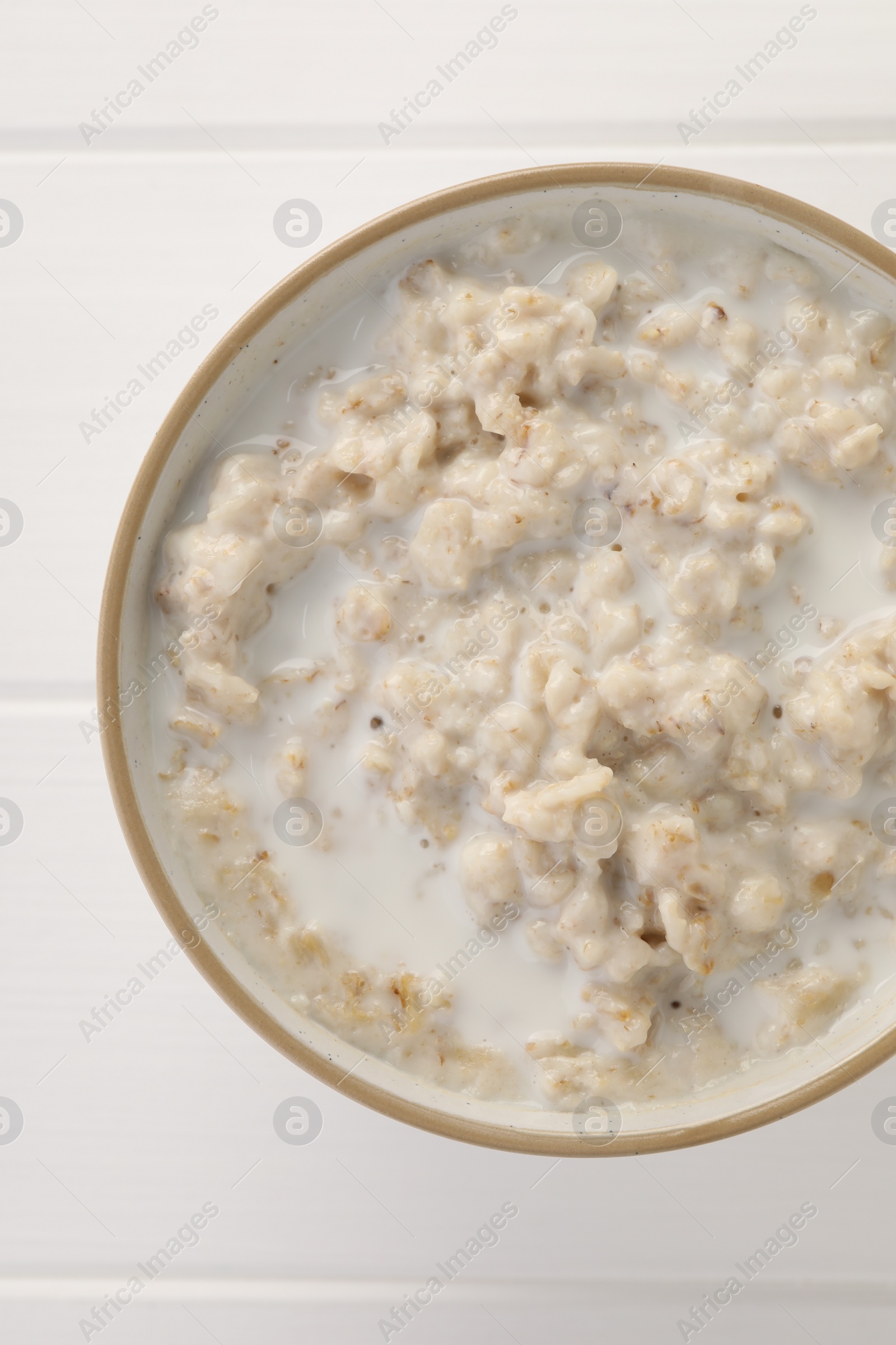 Photo of Tasty boiled oatmeal in bowl on white wooden table, top view