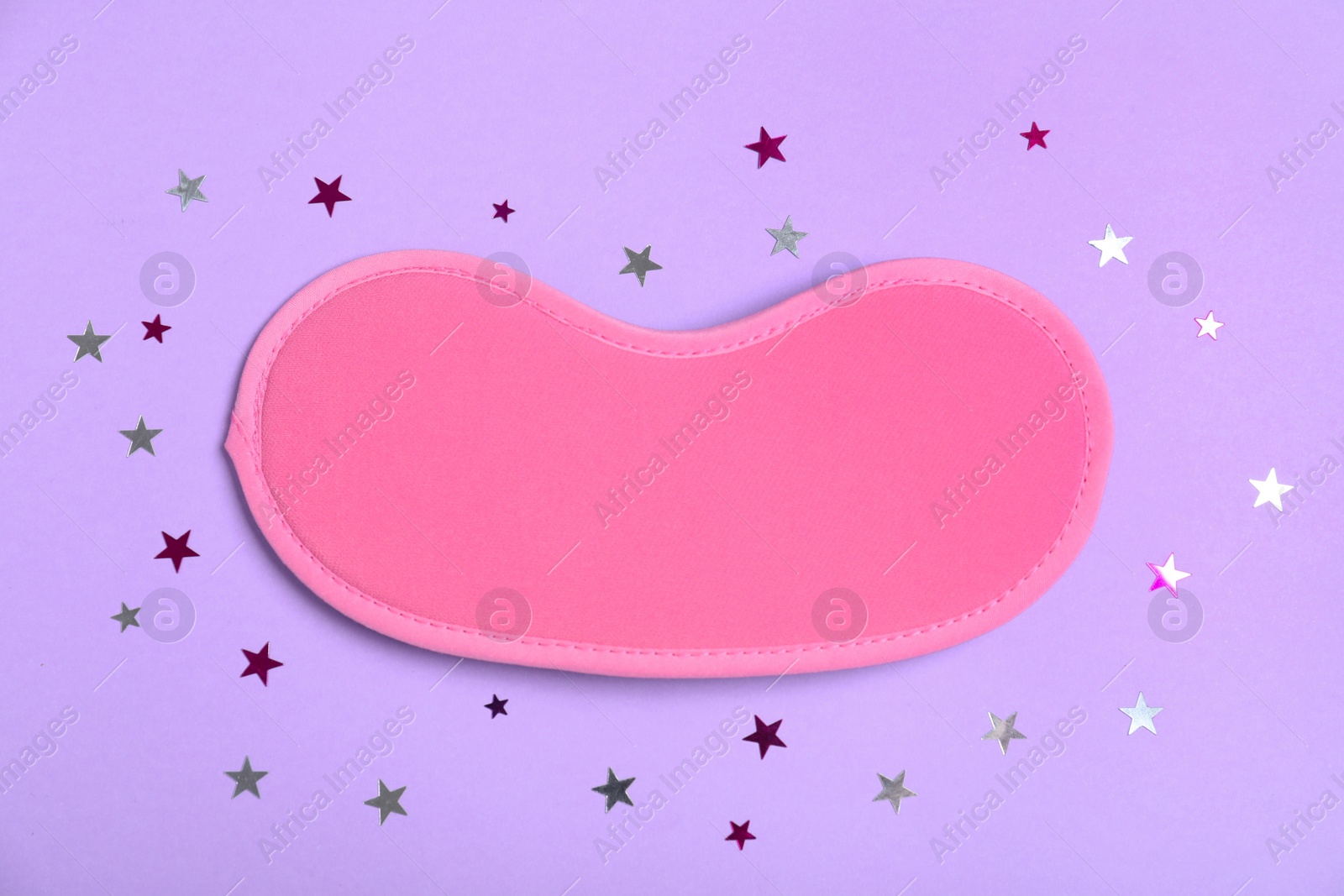 Photo of Pink sleeping mask and glitter on violet background, flat lay. Bedtime accessory