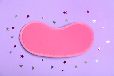Photo of Pink sleeping mask and glitter on violet background, flat lay. Bedtime accessory