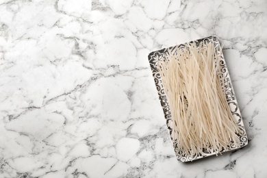 Photo of Plate with raw rice noodles on marble background, top view. Space for text