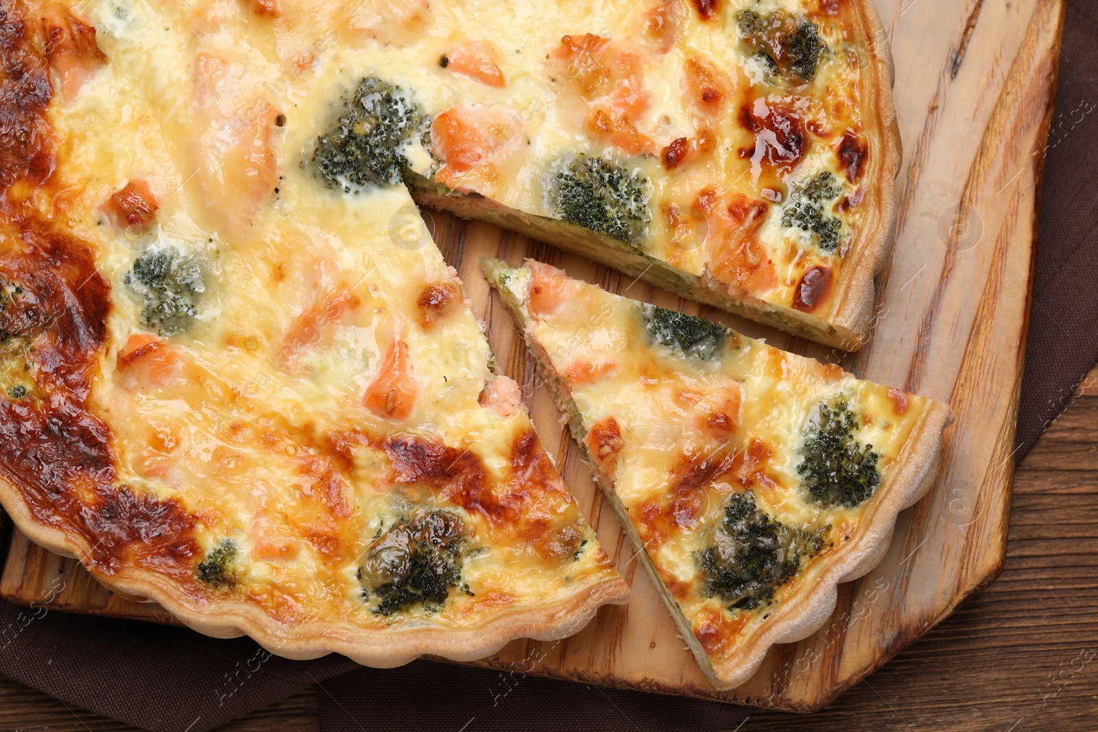 Photo of Delicious homemade quiche with salmon and broccoli on wooden table, top view