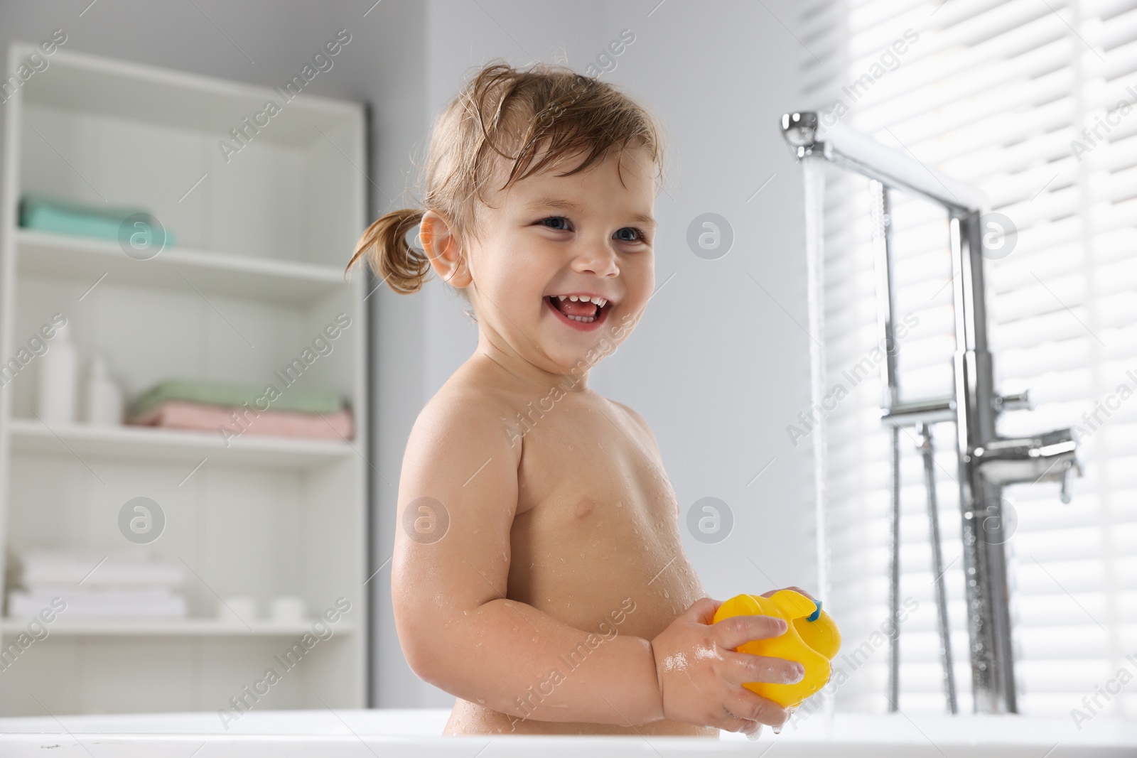 Photo of Happy little girl with toy in bathtub at home