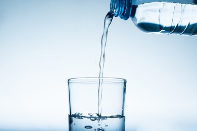 Photo of Pouring water from bottle into glass against grey background. Refreshing drink