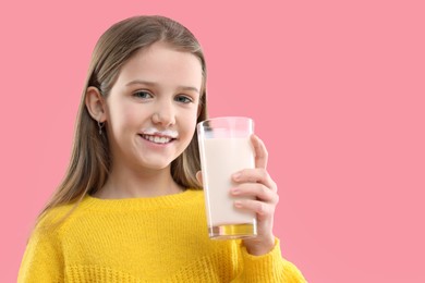 Photo of Happy little girl with milk mustache holding glass of tasty dairy drink on pink background. Space for text