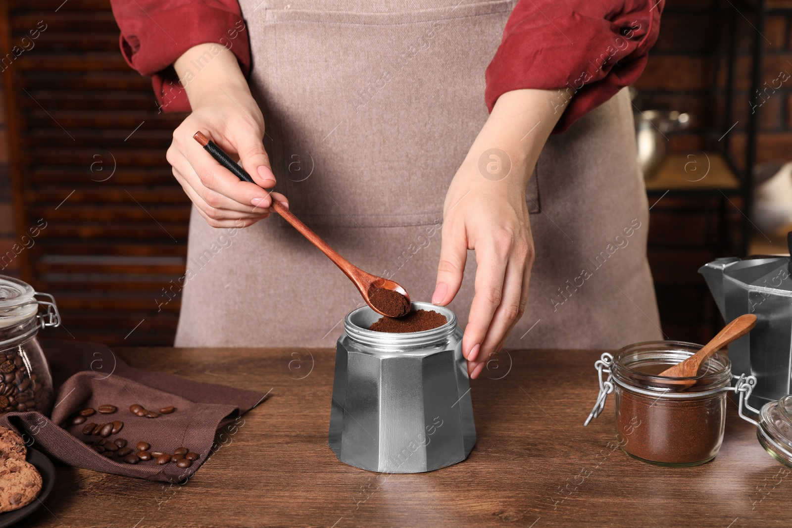 Photo of Woman putting ground coffee into moka pot at wooden table, closeup