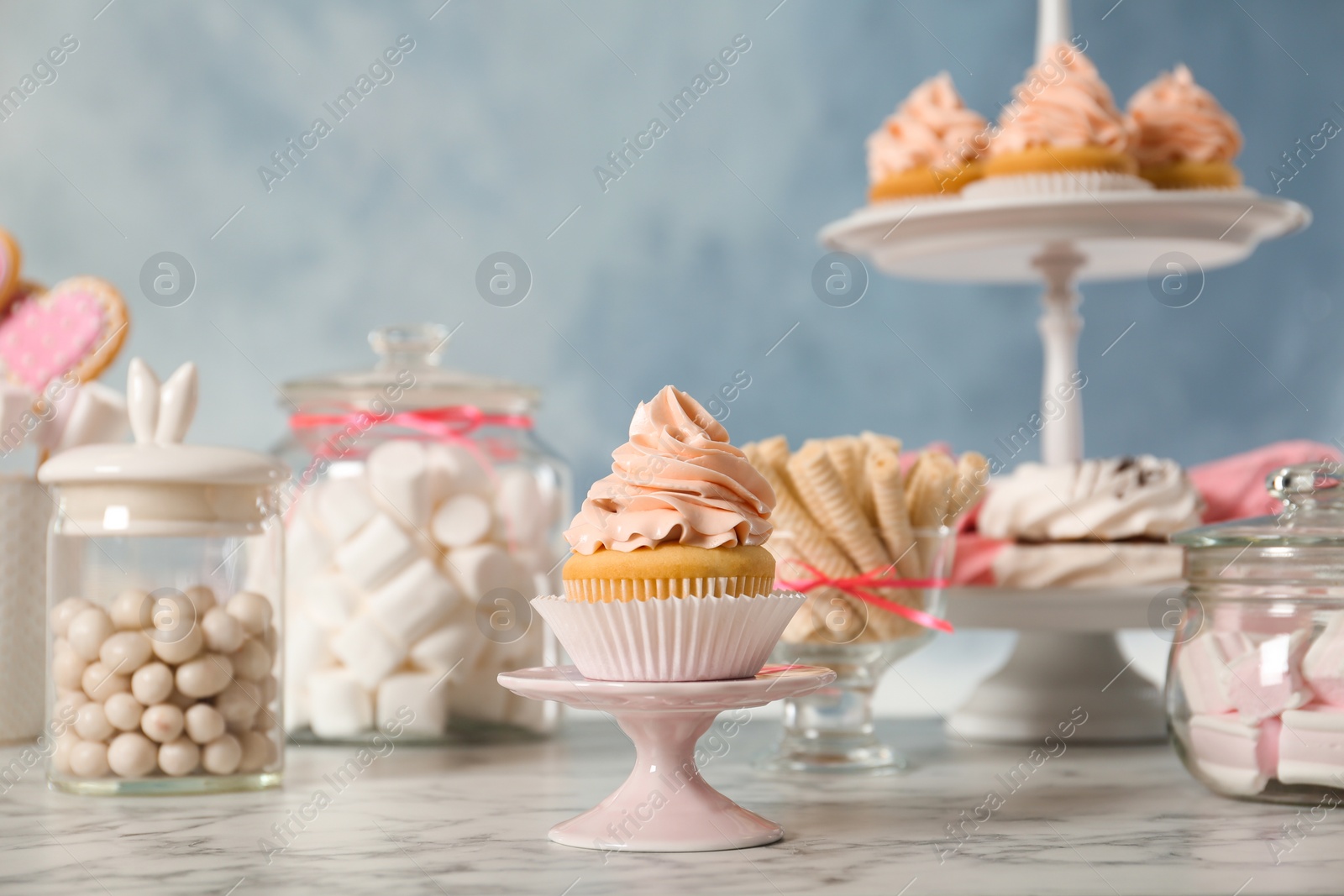 Photo of Stand with cupcake and other sweets on white marble table. Candy bar