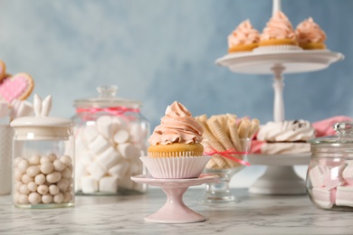 Stand with cupcake and other sweets on white marble table. Candy bar