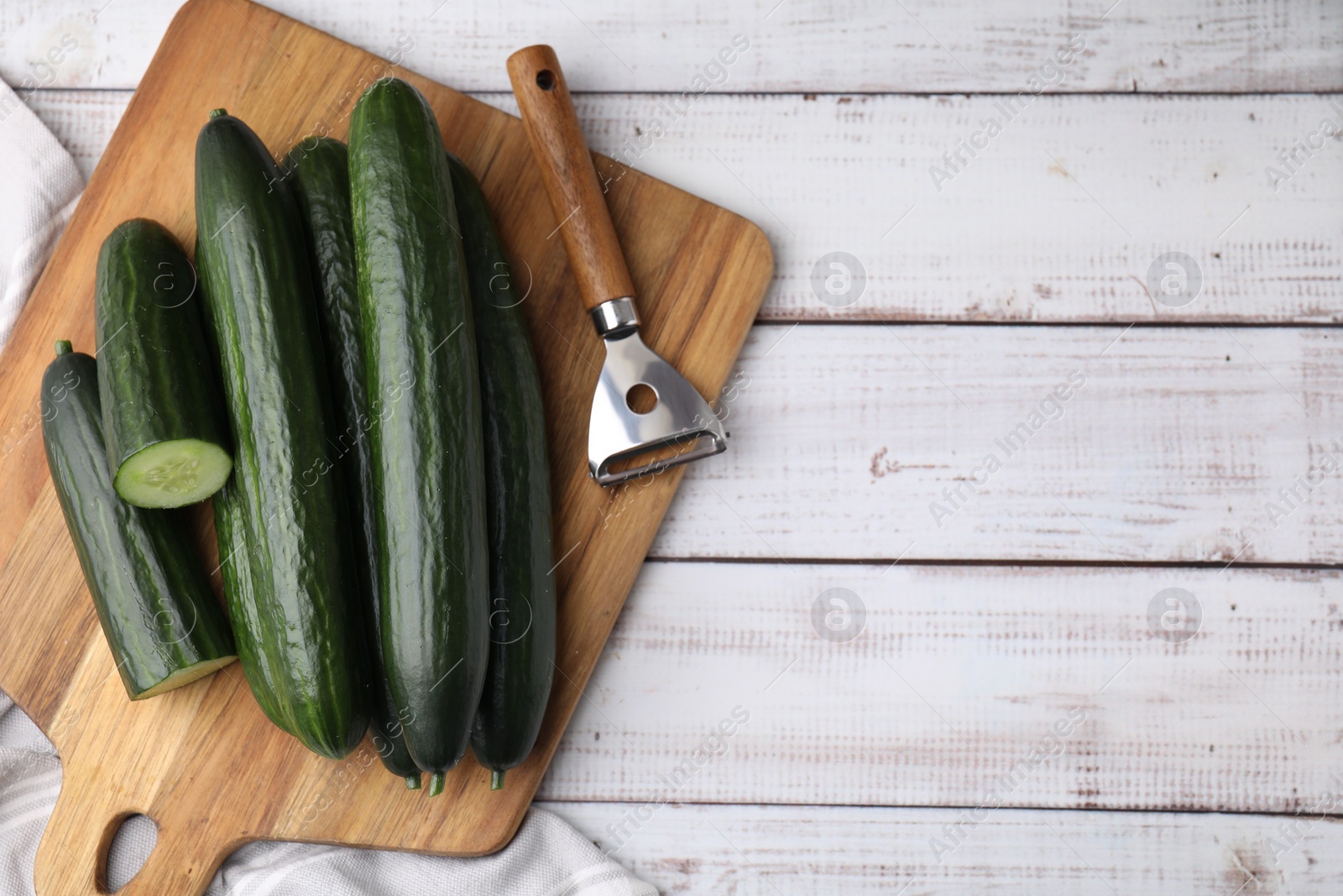 Photo of Fresh cucumbers and peeler on white wooden table, top view. Space for text