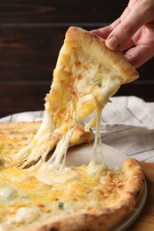 Photo of Woman taking piece of delicious cheese pizza at table, closeup