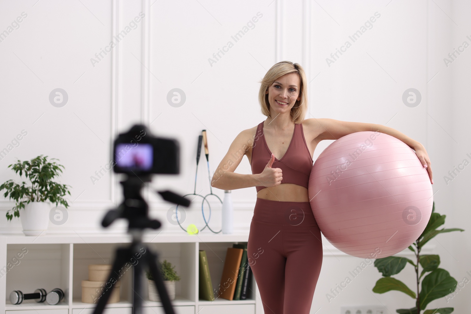 Photo of Smiling sports blogger holding fit ball while recording fitness lesson with camera at home