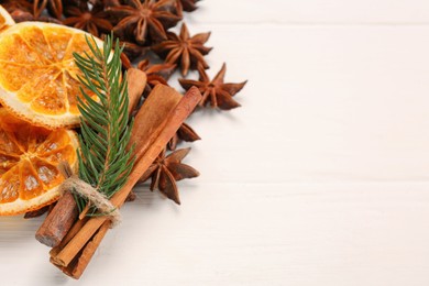 Dry orange slices, cinnamon sticks, fir branch and anise stars on white wooden table, space for text