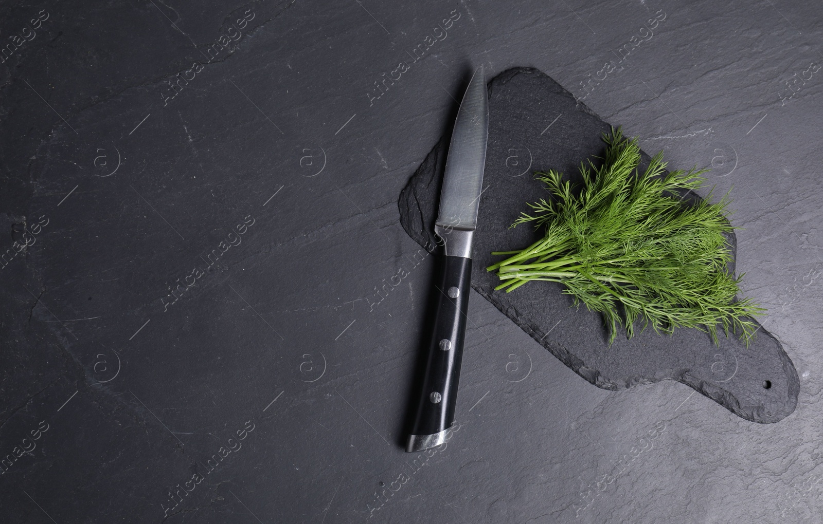 Photo of Sprigs of fresh green dill and knife on black table, top view. Space for text