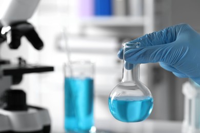 Photo of Scientist holding flask with light blue liquid in laboratory, closeup. Space for text