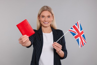 Immigration. Happy woman with passport and flag of United Kingdom on gray background
