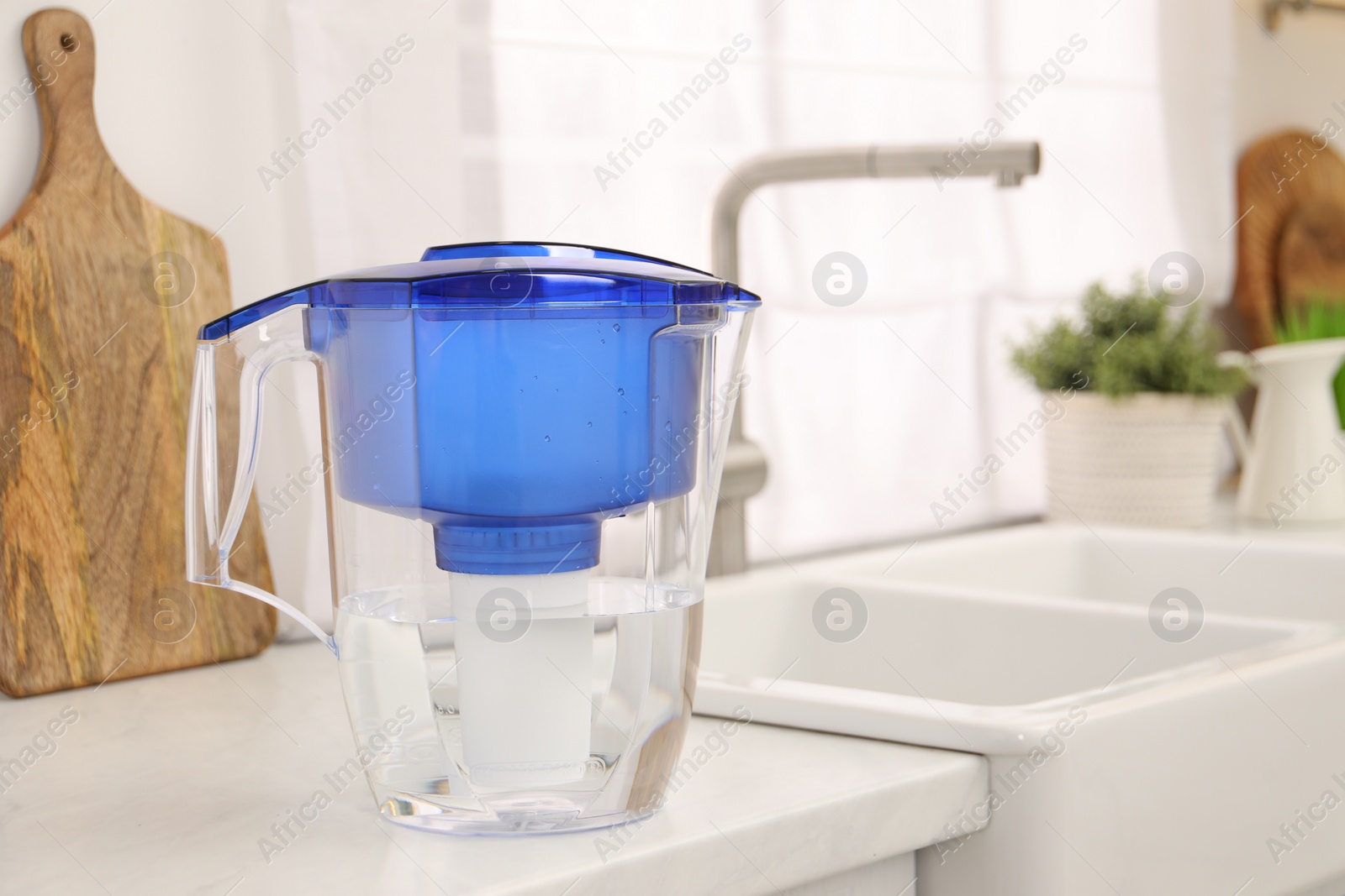 Photo of Water filter jug on white countertop in kitchen, space for text