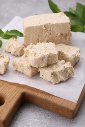 Photo of Pieces of tasty halva and mint leaves on light grey table, closeup