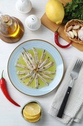 Photo of Tasty pickled anchovies with spices and products on white wooden table, flat lay