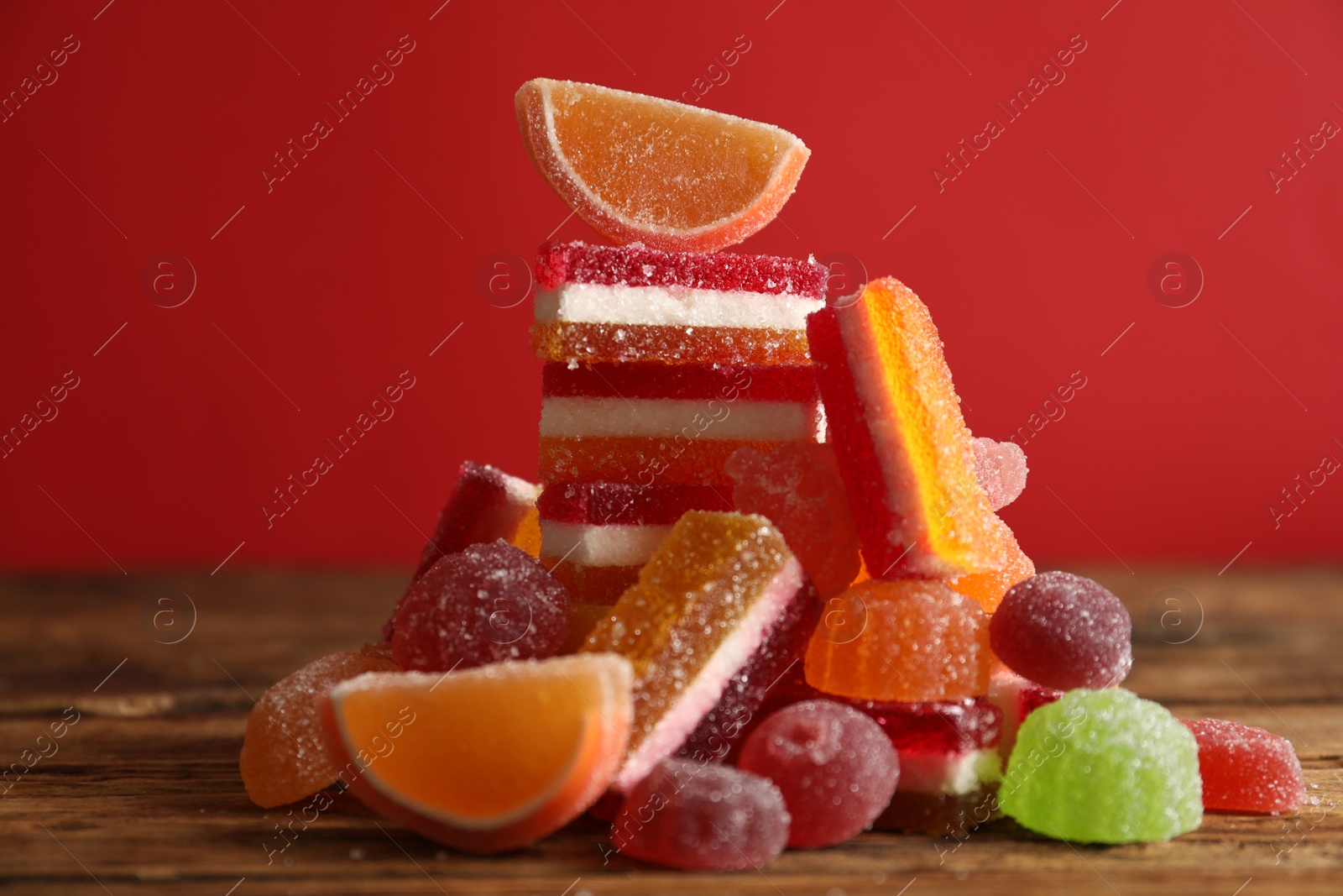 Photo of Delicious jelly candies on wooden table against red background, closeup