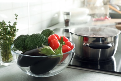 Photo of Bowl of vegetables near pot with boiling water on stove