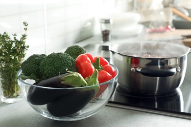 Bowl of vegetables near pot with boiling water on stove