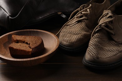 Photo of Poverty. Old shoes, bag and pieces of bread on wooden table