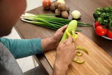 Man peeling zucchini at kitchen table, closeup. Preparing vegetable