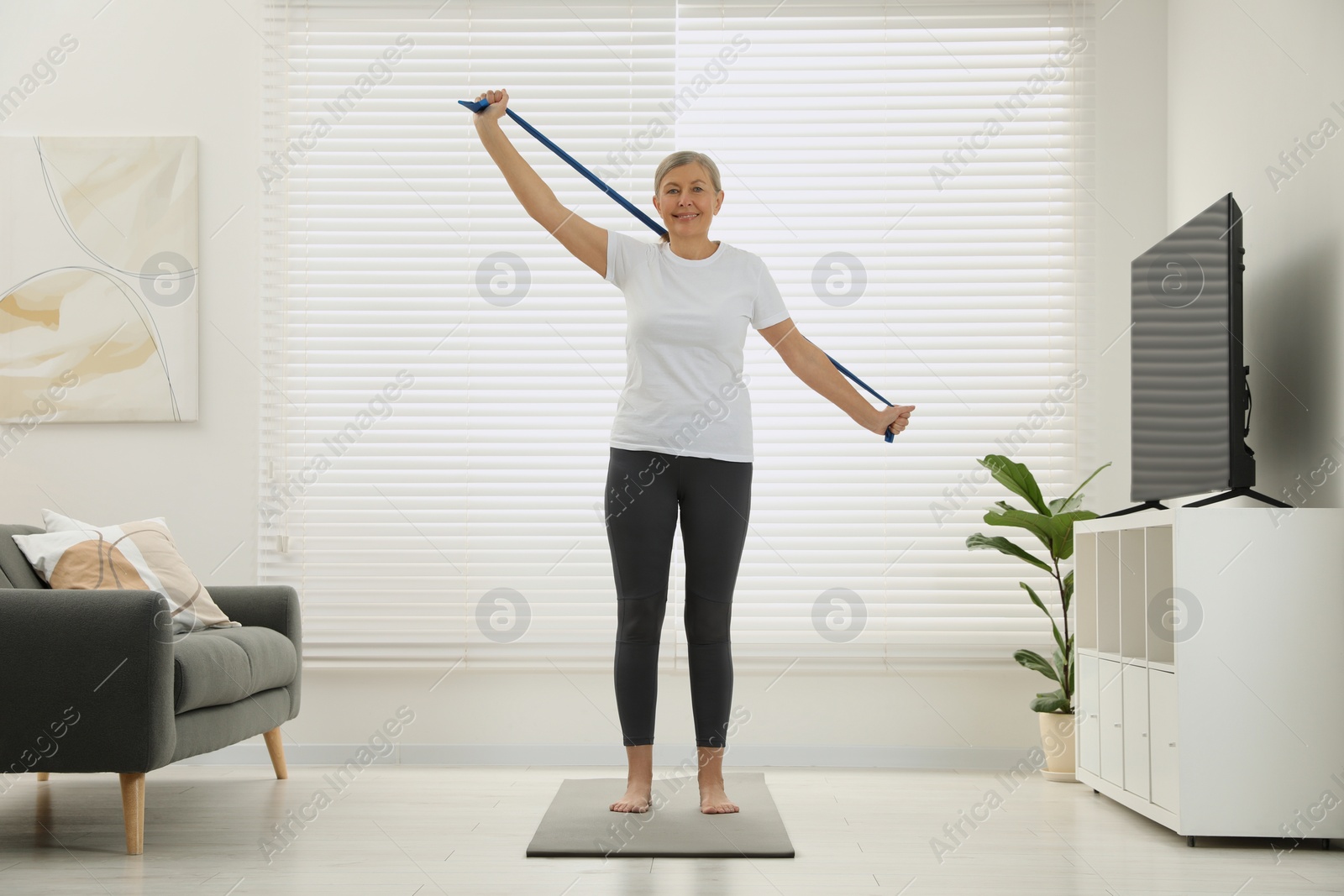 Photo of Senior woman doing exercise with fitness elastic band on mat at home