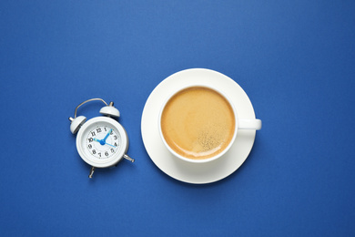 Photo of Classic black coffee and alarm clock on blue background, top view. Color of the year 2020