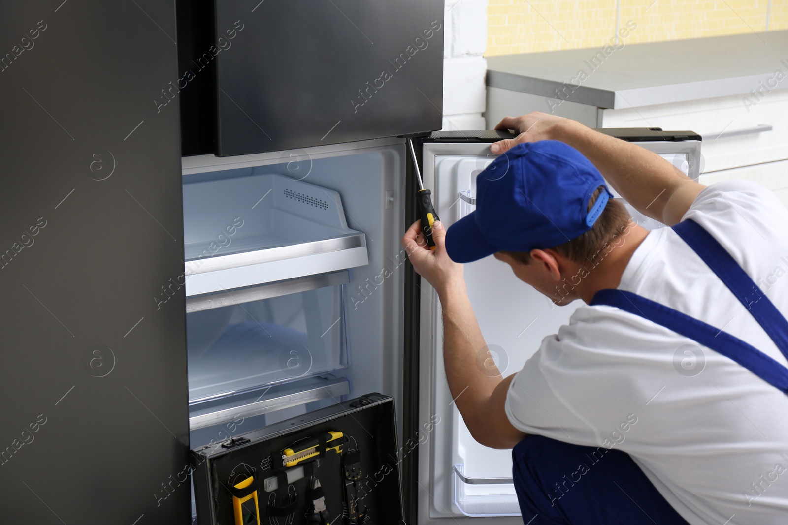 Photo of Male technician with screwdriver repairing refrigerator in kitchen