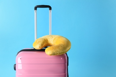 Photo of Pink suitcase and travel pillow on light blue background, space for text