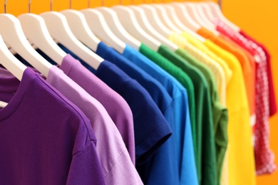 Photo of Rainbow clothes on hangers against color background, closeup