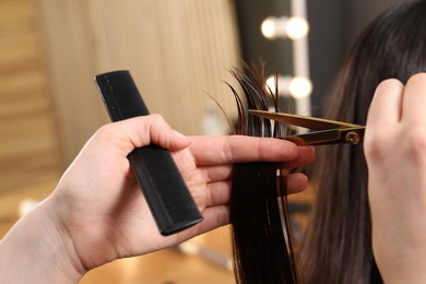 Photo of Hairdresser cutting client's hair with scissors in salon, closeup