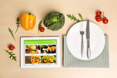 Photo of Modern tablet with open page for online food ordering, vegetables, spices, plate and cutlery on wooden table, flat lay. Concept of delivery service