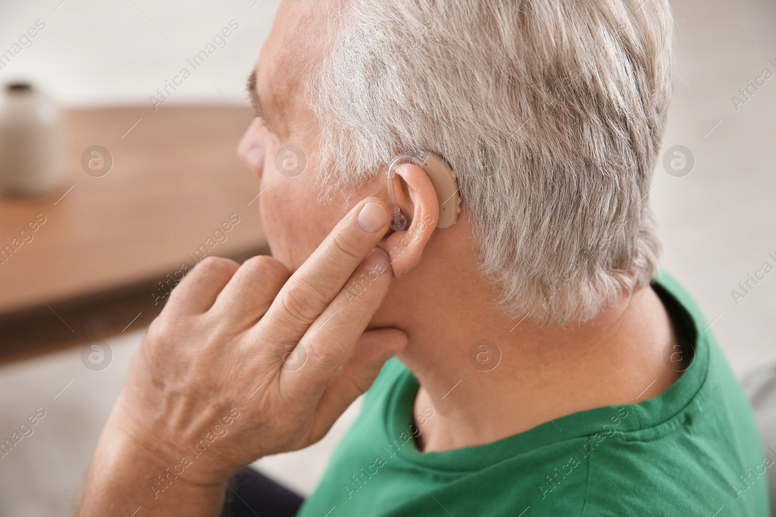 Photo of Mature man adjusting hearing aid at home, closeup