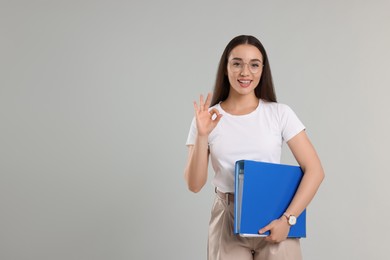 Photo of Happy woman with folder showing OK gesture on light gray background, space for text