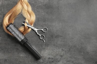 Photo of Professional hairdresser scissors, brush and strand of blonde hair on grey background, top view