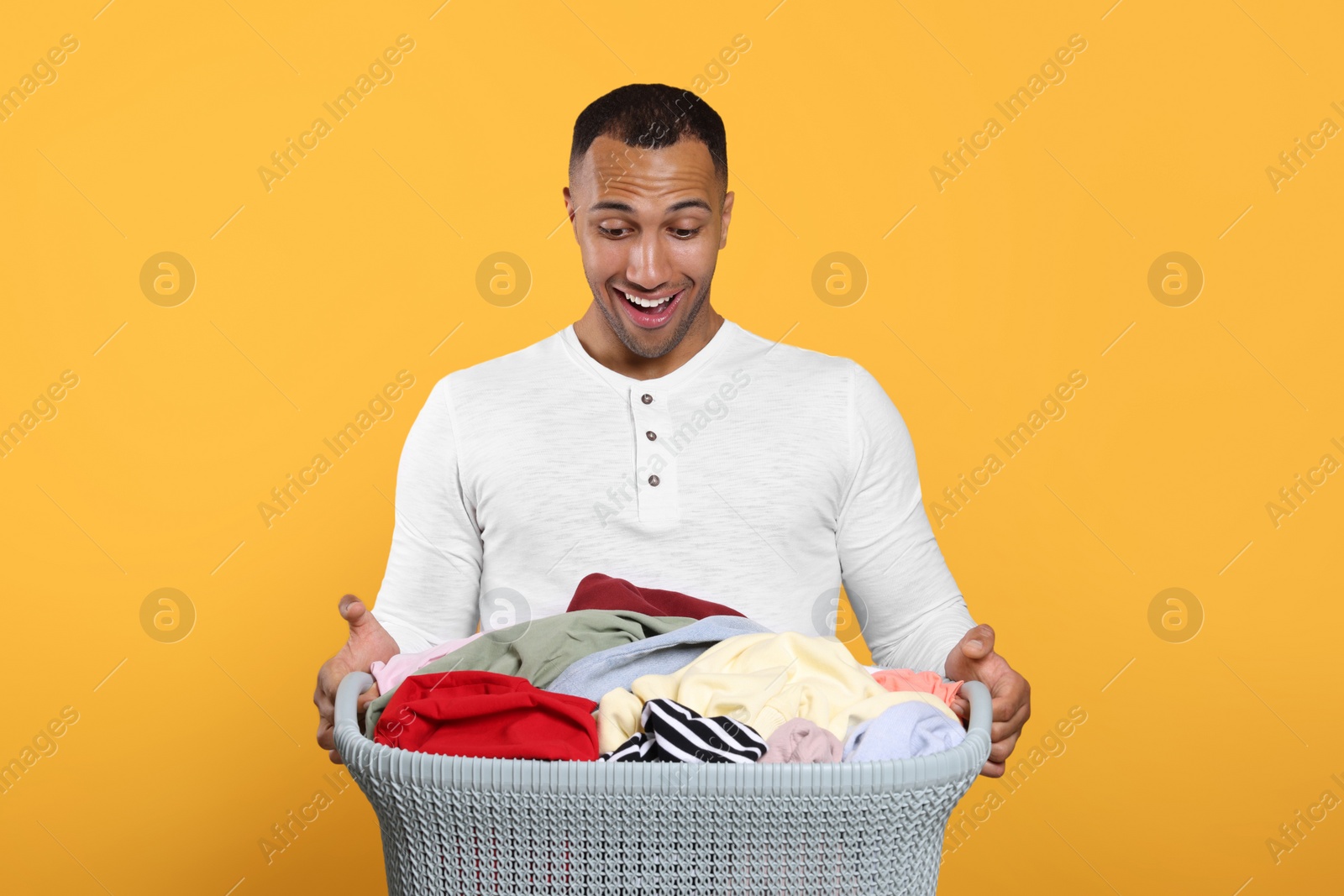 Photo of Emotional man with basket full of laundry on orange background