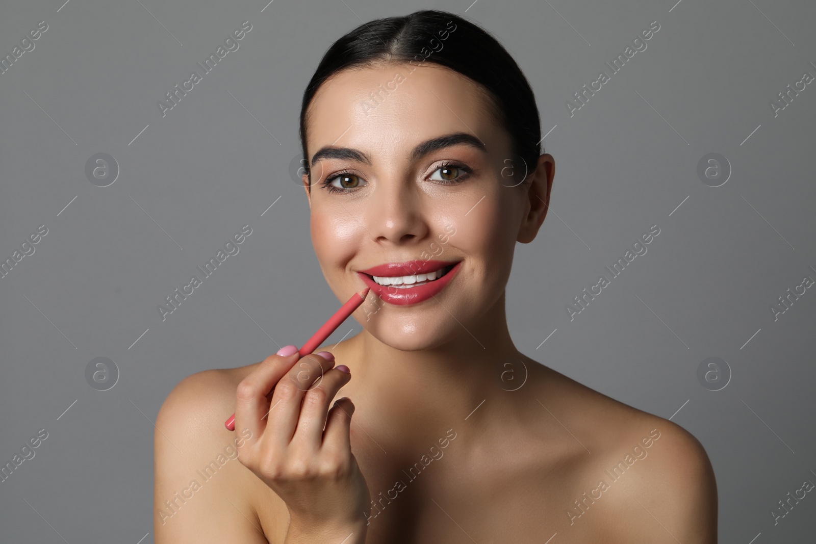 Photo of Pretty young woman applying beautiful pink lip pencil on grey background