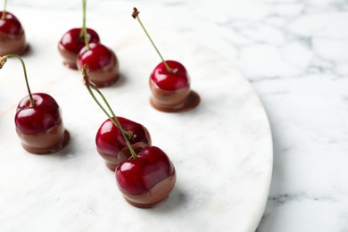 Photo of Sweet chocolate dipped cherries on white marble table, closeup. Space for text