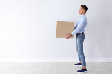 Photo of Full length portrait of young man carrying heavy cardboard box near white wall. Posture concept