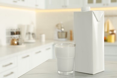 Photo of Carton box and glass of milk on table in kitchen, space for text