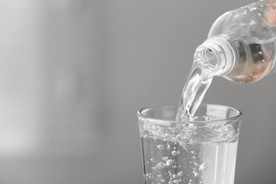 Pouring water from bottle into glass on light grey background, closeup. Space for text