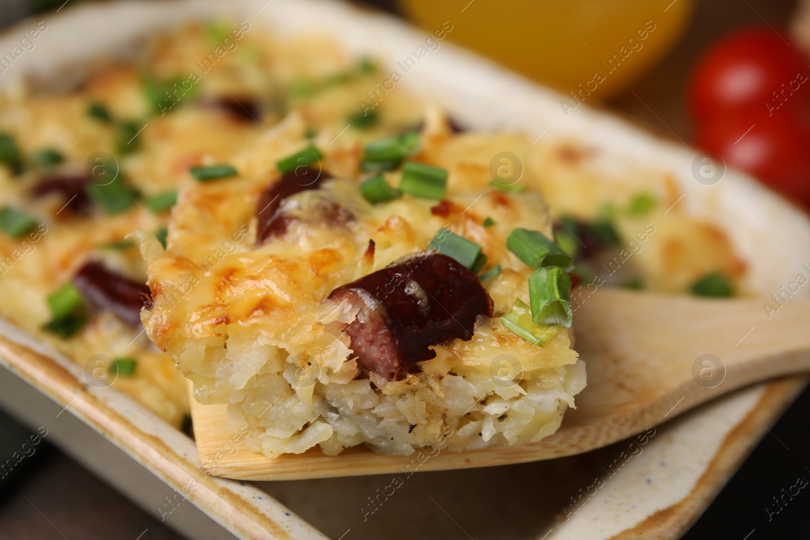 Photo of Taking piece of tasty sausage casserole from baking dish at table, closeup